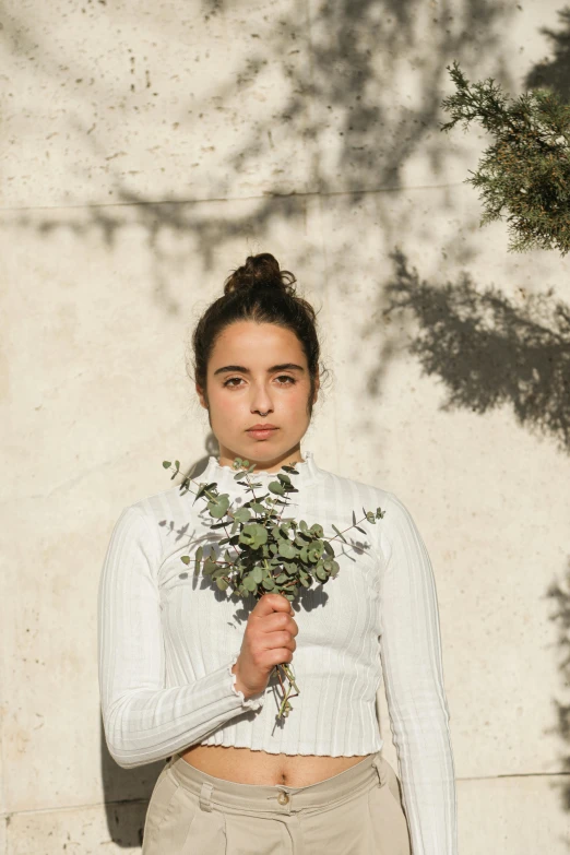 a woman holding leaves while wearing a white top