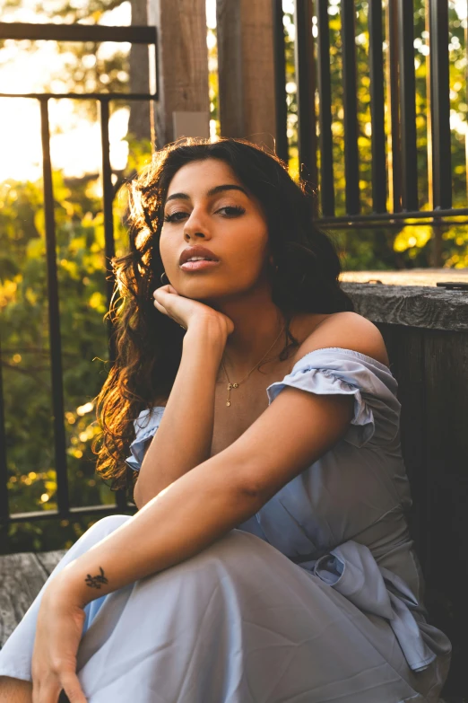 a woman sitting in a dress in front of a fence