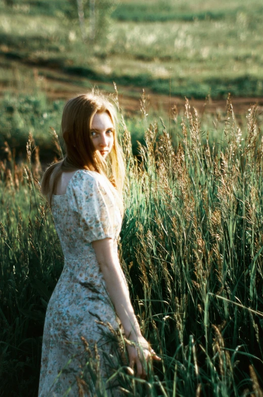 a girl wearing a floral dress stands in tall grass
