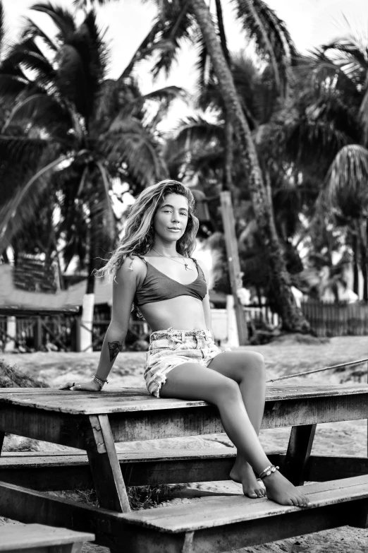 a woman wearing a bikini top and a flower skirt sitting on a picnic bench