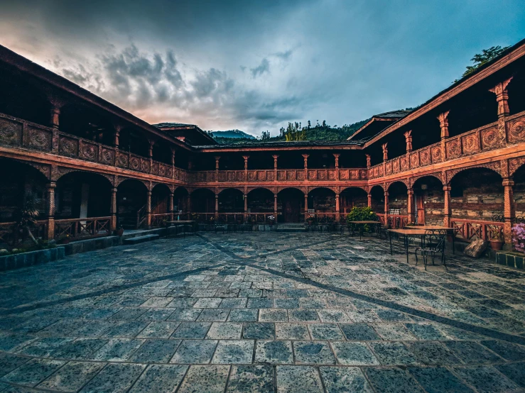 a stone courtyard is empty at dusk with dark clouds