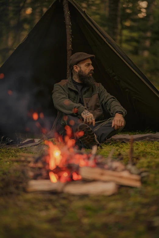 a man sits by a campfire in front of a tent