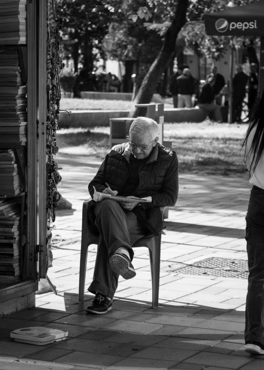 an elderly man sitting at a bench reading a book