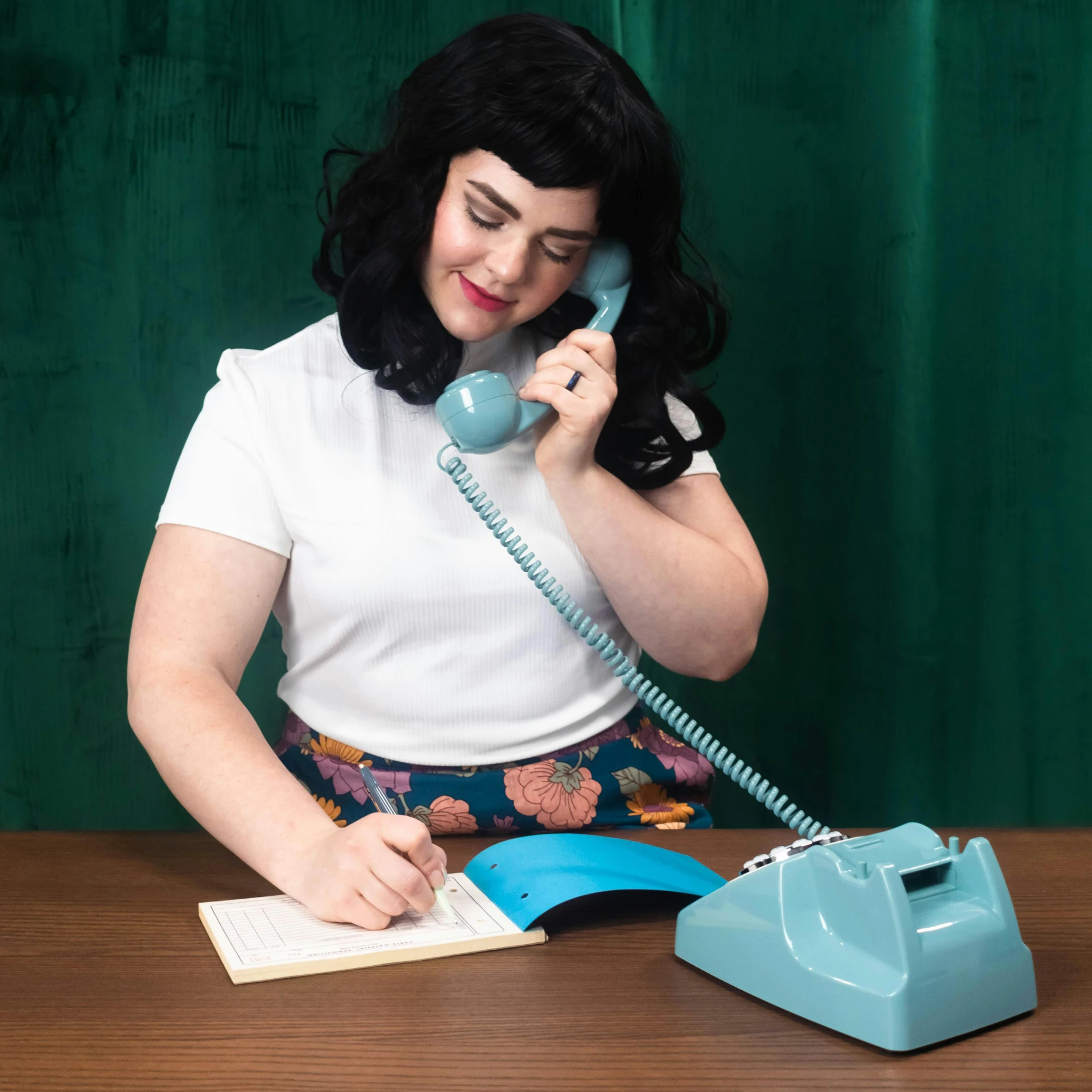 a woman in a skirt, sitting at a table talking on the phone