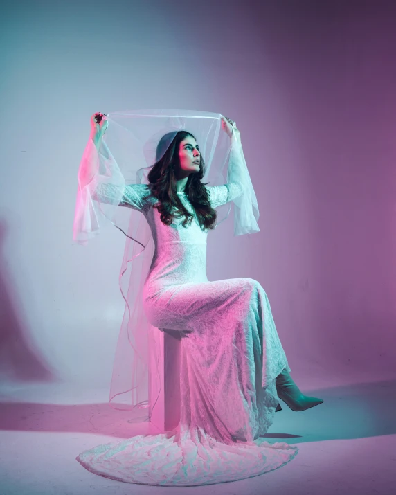 a woman in white sitting on a stool with her arm up and holding a piece of cloth