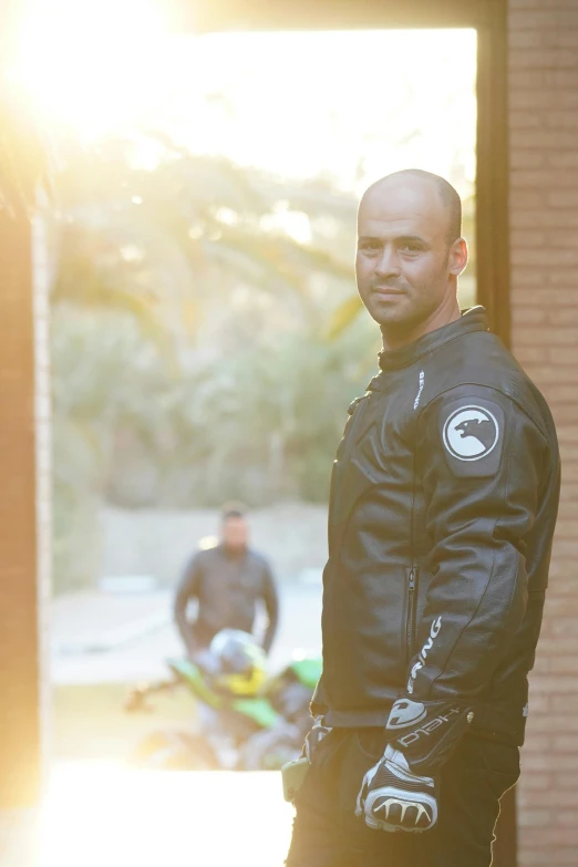 a man in black motorcycle outfit standing by some buildings