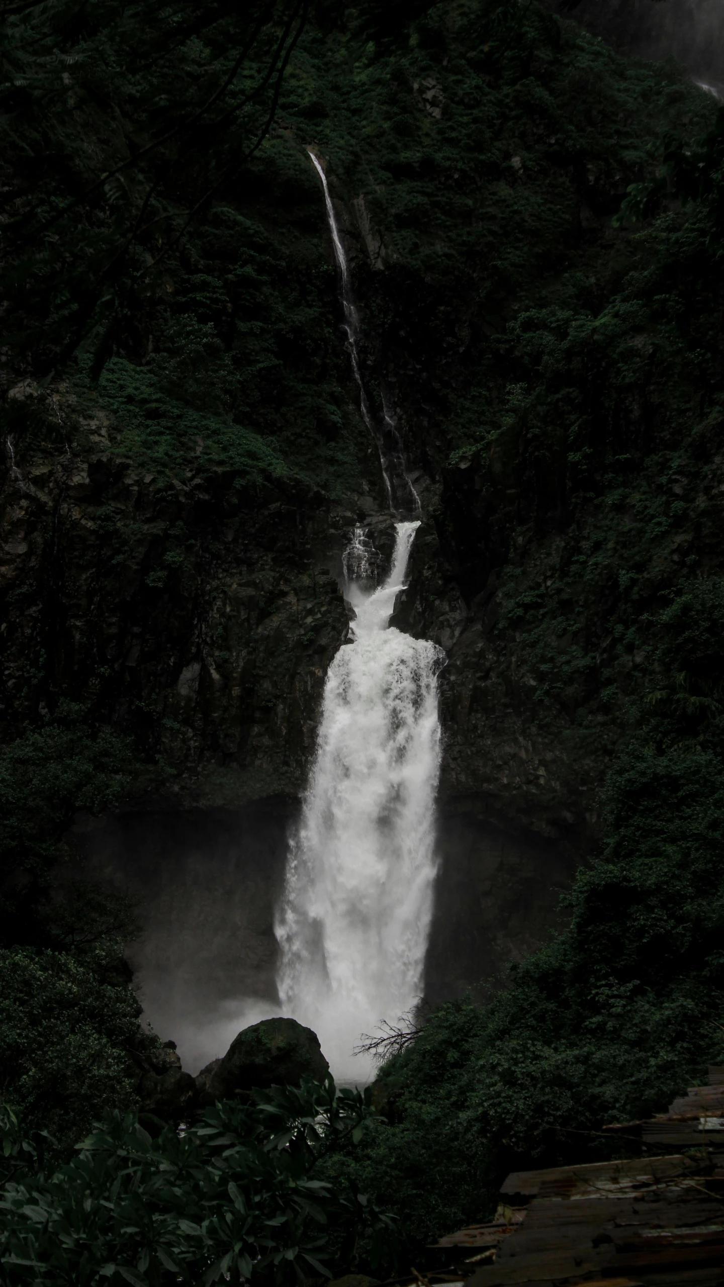 water flows over rocks towards a river beneath a large waterfall