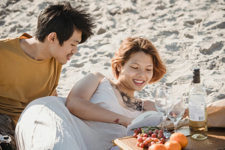 a couple enjoys wine and gs while sitting on a blanket at the beach