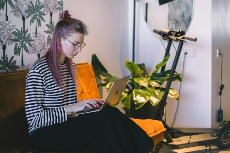 a young woman sits on an orange couch and uses a laptop