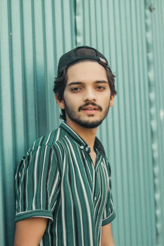 a man is wearing a cap in front of a metal wall