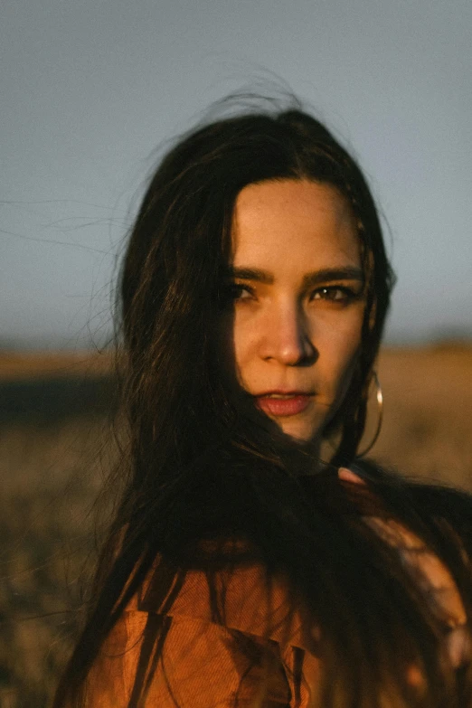 a person standing in some grass with the sun low on her face