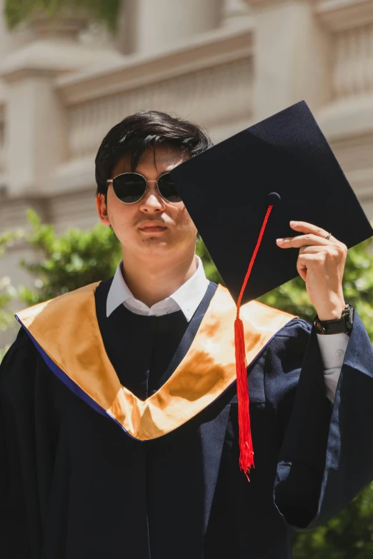 young man in black and gold graduation gown holding up his cap