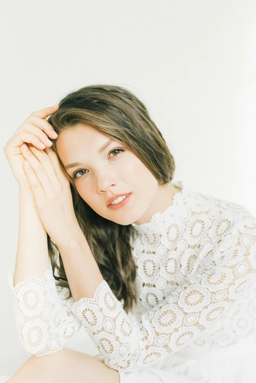 a woman in a white top and holding her hands near her hair