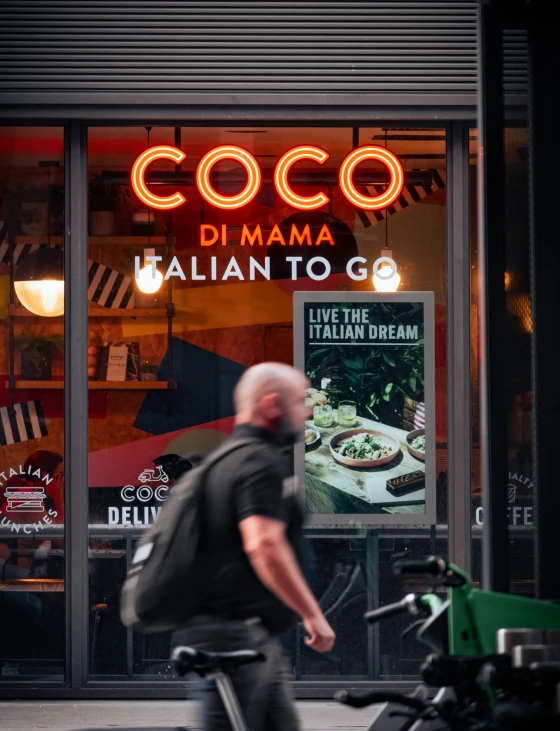 a man riding a bike past a italian restaurant sign
