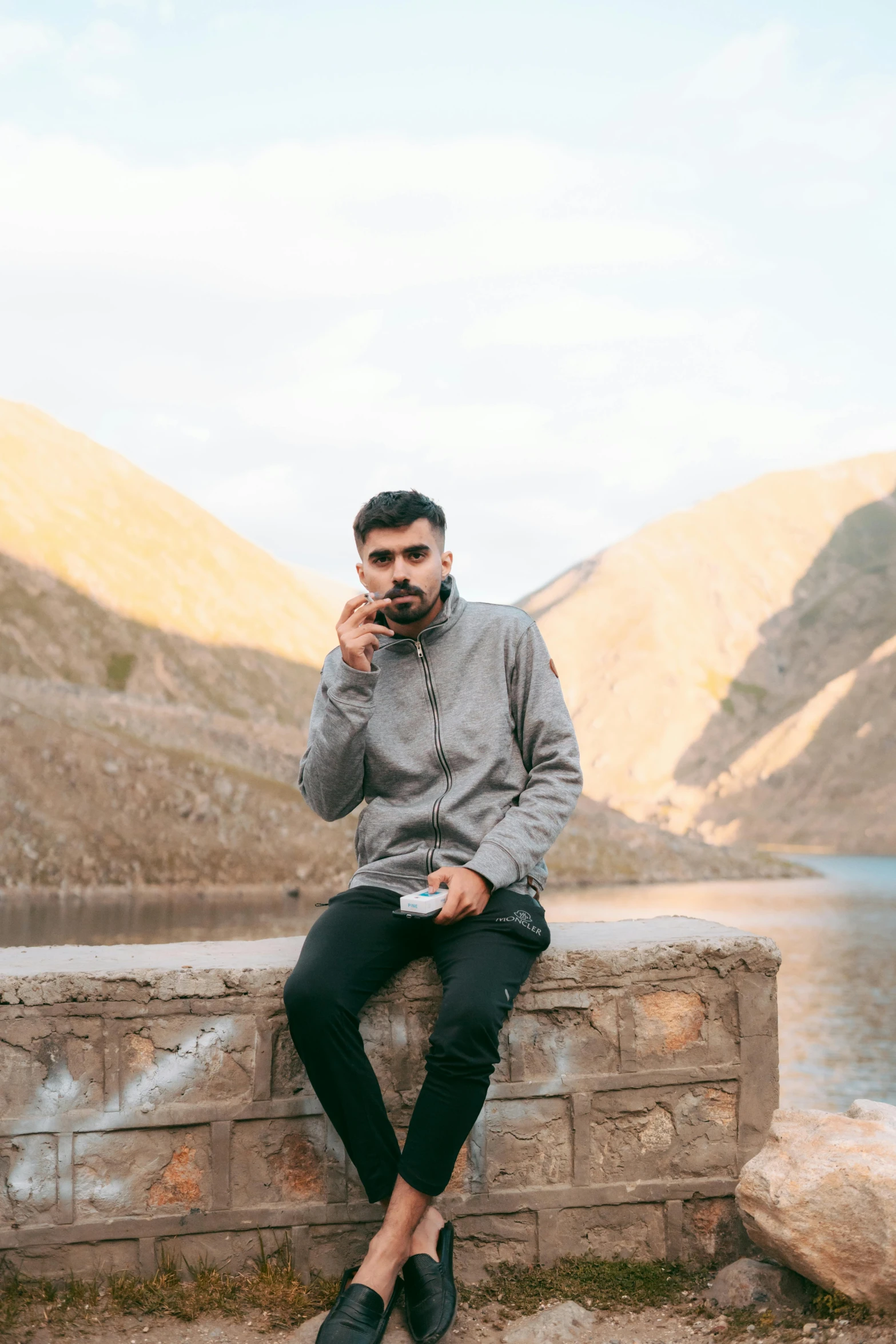 a man is sitting on a wall while talking on a cell phone