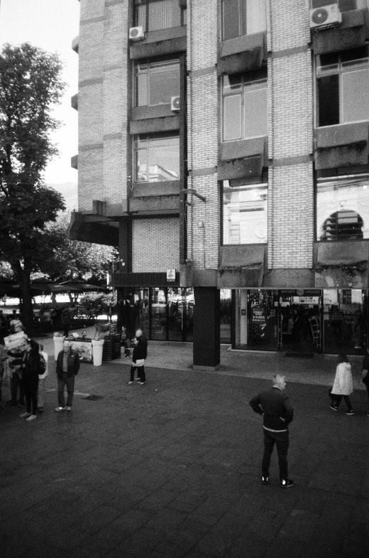 people gather outside a tall brick building near a park