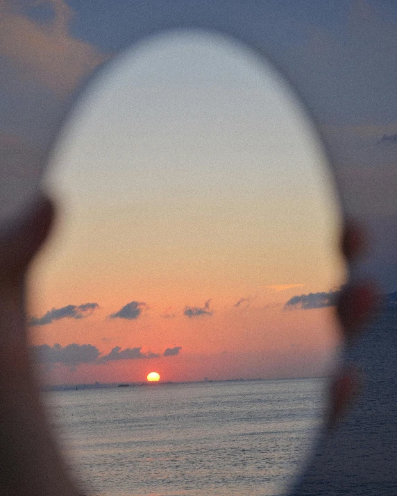 a person is looking through a magnifying glass at a sunset