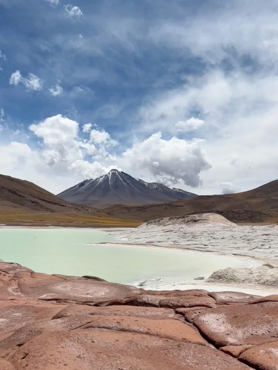 a blue lagoon in the desert with snow capped mountains in the distance