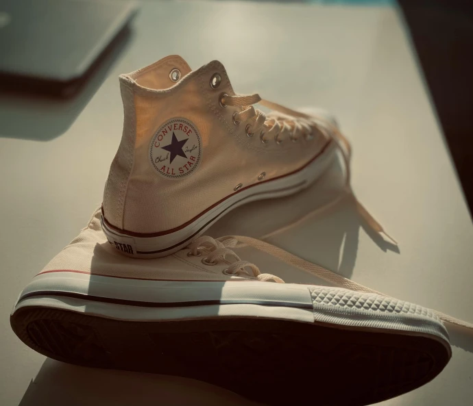 a pair of converse sneakers on a table with a laptop nearby