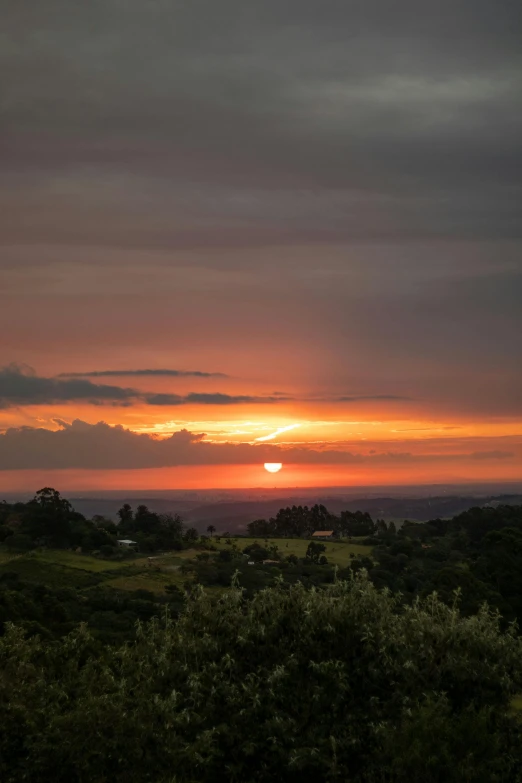 the sun sets behind a cloudy sky over a field