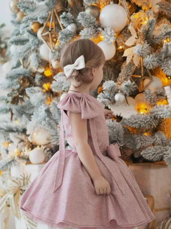 a girl with a bow on her head is standing in front of a christmas tree