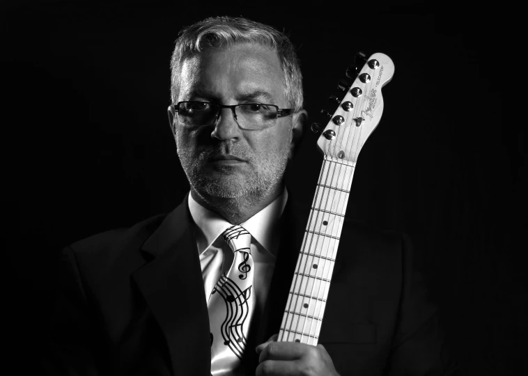 a man holds up his guitar while wearing glasses