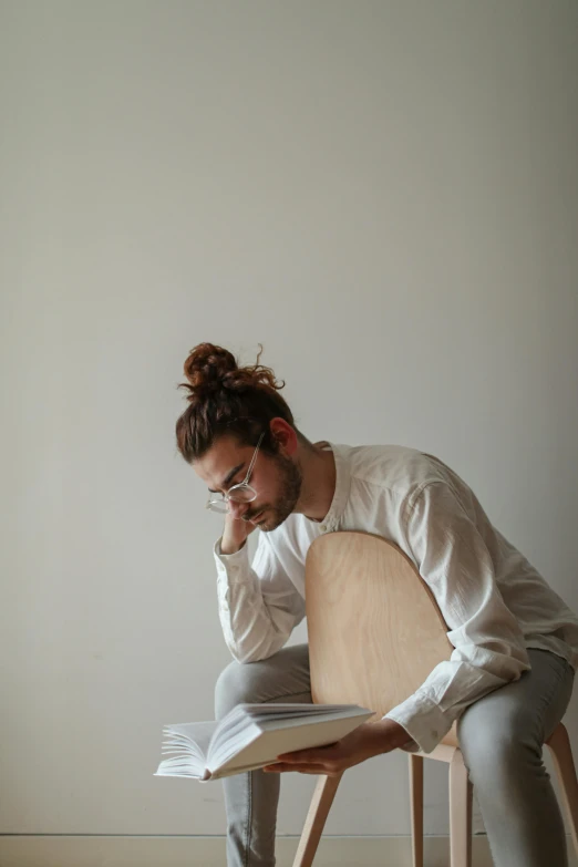 a man in glasses reading on a wooden chair