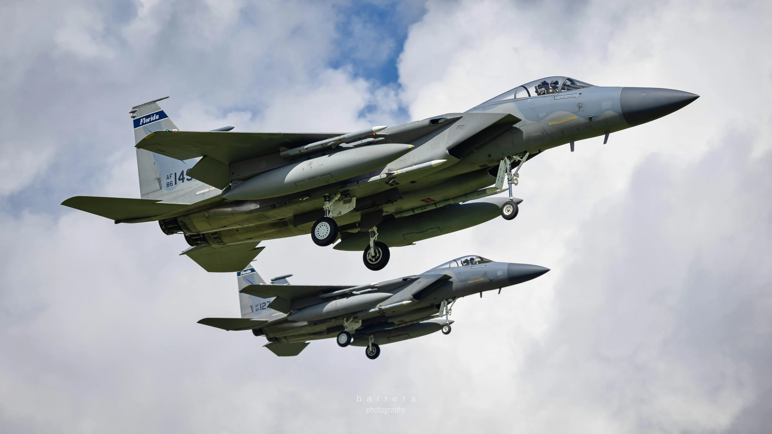 two fighter jets are flying in a blue cloudy sky