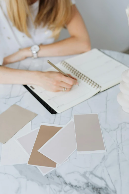 a woman with white hair is writing in a notebook with a notepad on top of her and some beige pieces