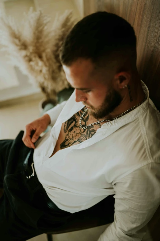 man with tattoos sitting on a bench in a white shirt and jeans
