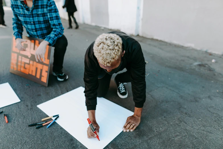 a man writing on a paper while sitting on the ground