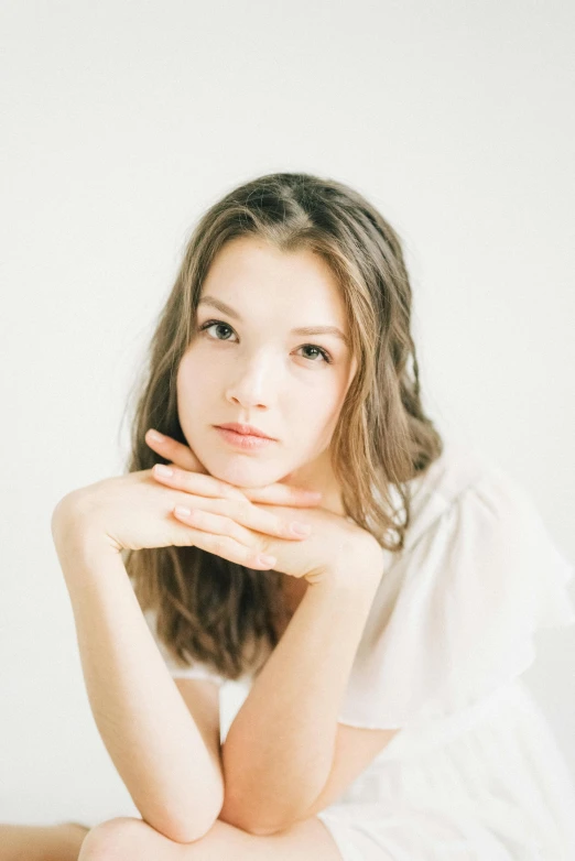 a beautiful young woman with long hair in white sitting in front of a wall