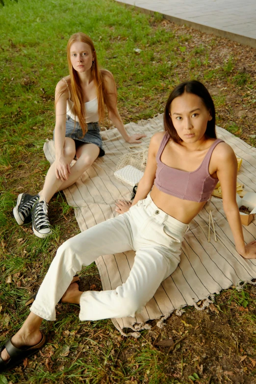 two girls sitting on a blanket in a park