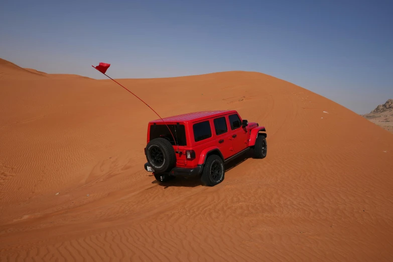 a red jeep with a kite in the middle of a desert