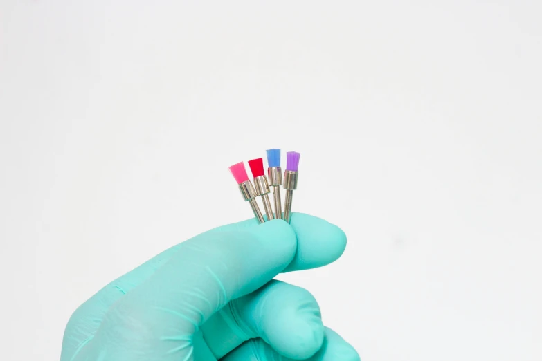 a hand wearing gloves holding three colored tooth brushes