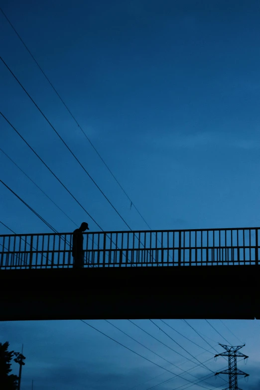 man with umbrella walking across a high bridge in the evening