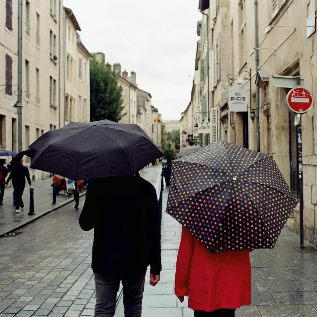 two people holding umbrellas as they walk on the sidewalk