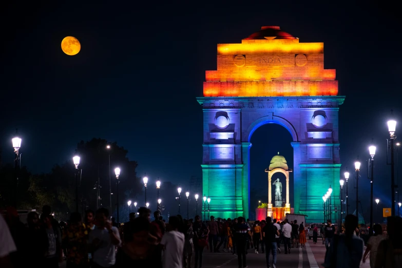 a crowd of people walk near an illuminated arch