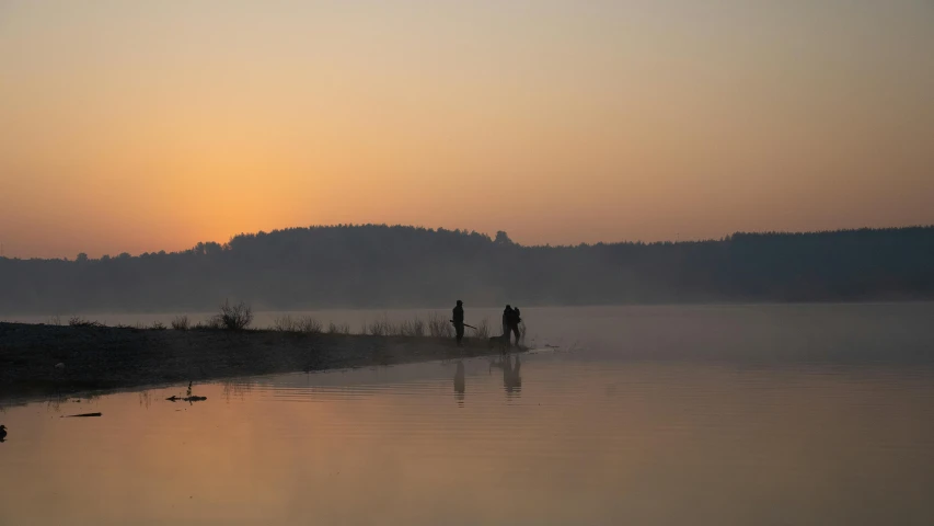 people stand in water in front of a hill