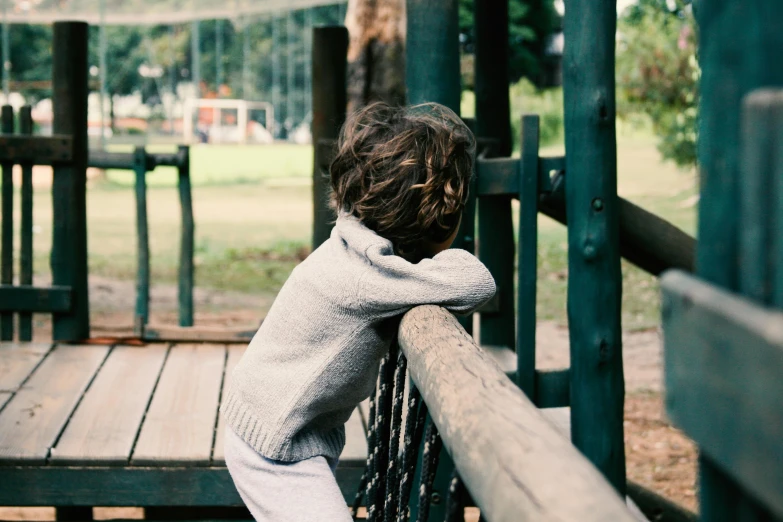 a small child wearing a sweater leaning on a railing