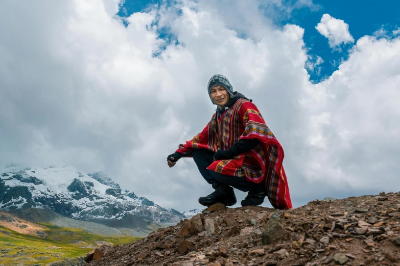 a man in red sits on the rocks in front of mountains