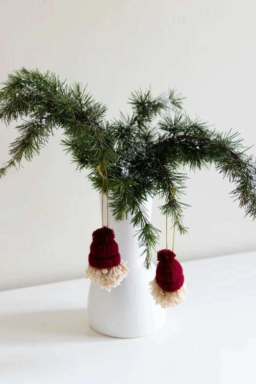 a white vase with a nch of a pine and some yarn balls