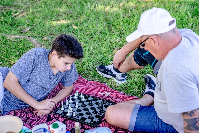 a boy plays chess while another man stands with his hand