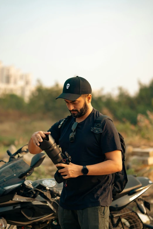 a man standing in front of a motorcycle with a cap and a backpack