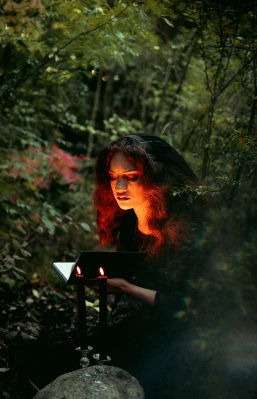 a woman is sitting down in the woods with her tablet