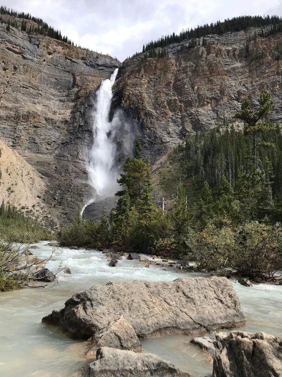 a tall waterfall is shown near some trees