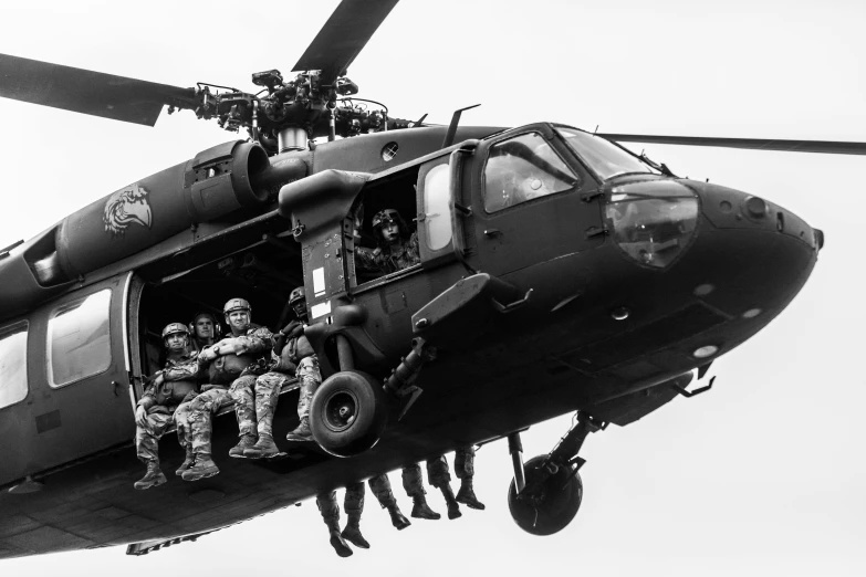 a black and white image of several soldiers on the front steps of an army helicopter