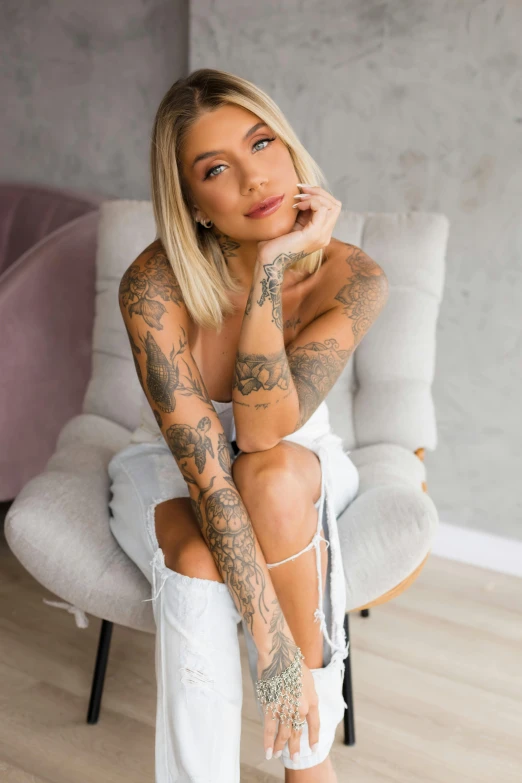 a woman with tattoos on her arm and legs, sitting in an armchair