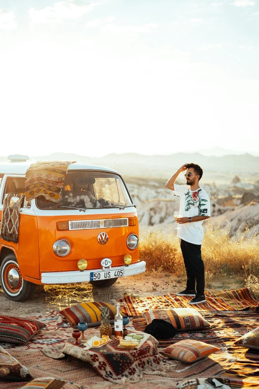 a person near a van sitting in the sand with a surfboard