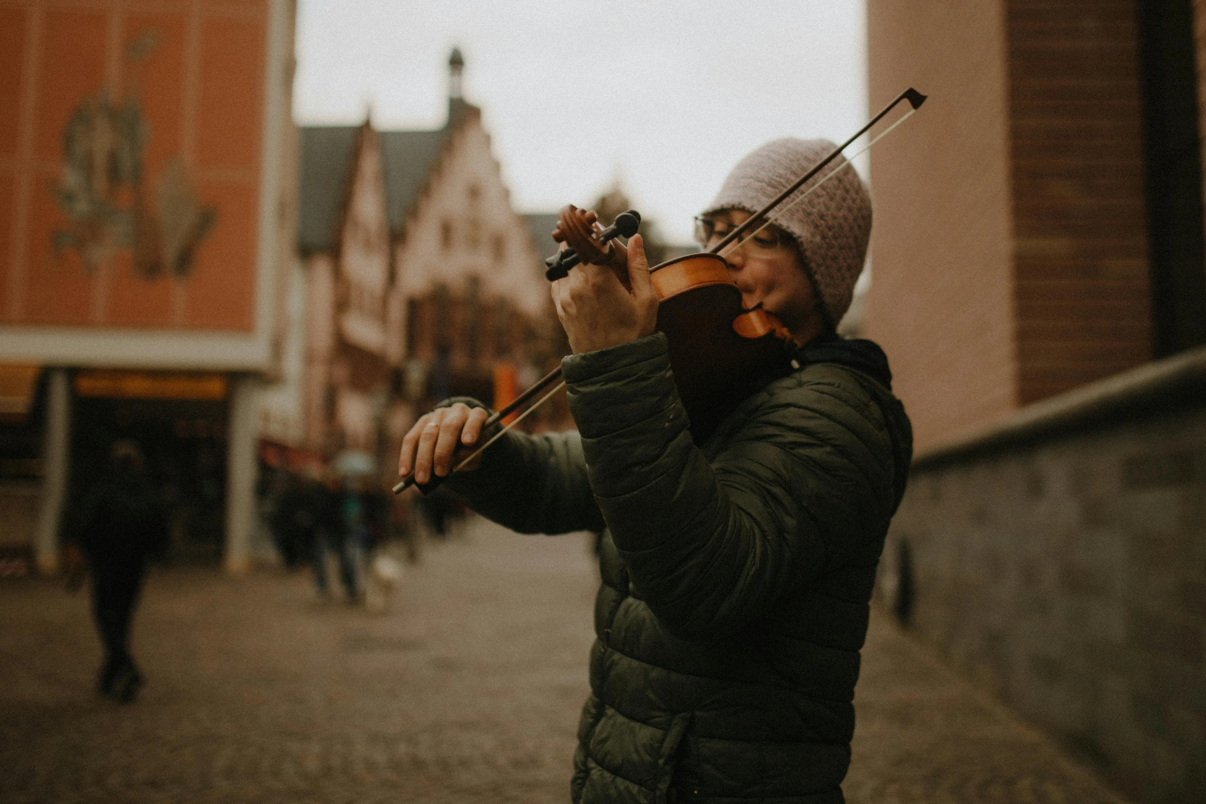 a man playing violin on the street next to brick buildings